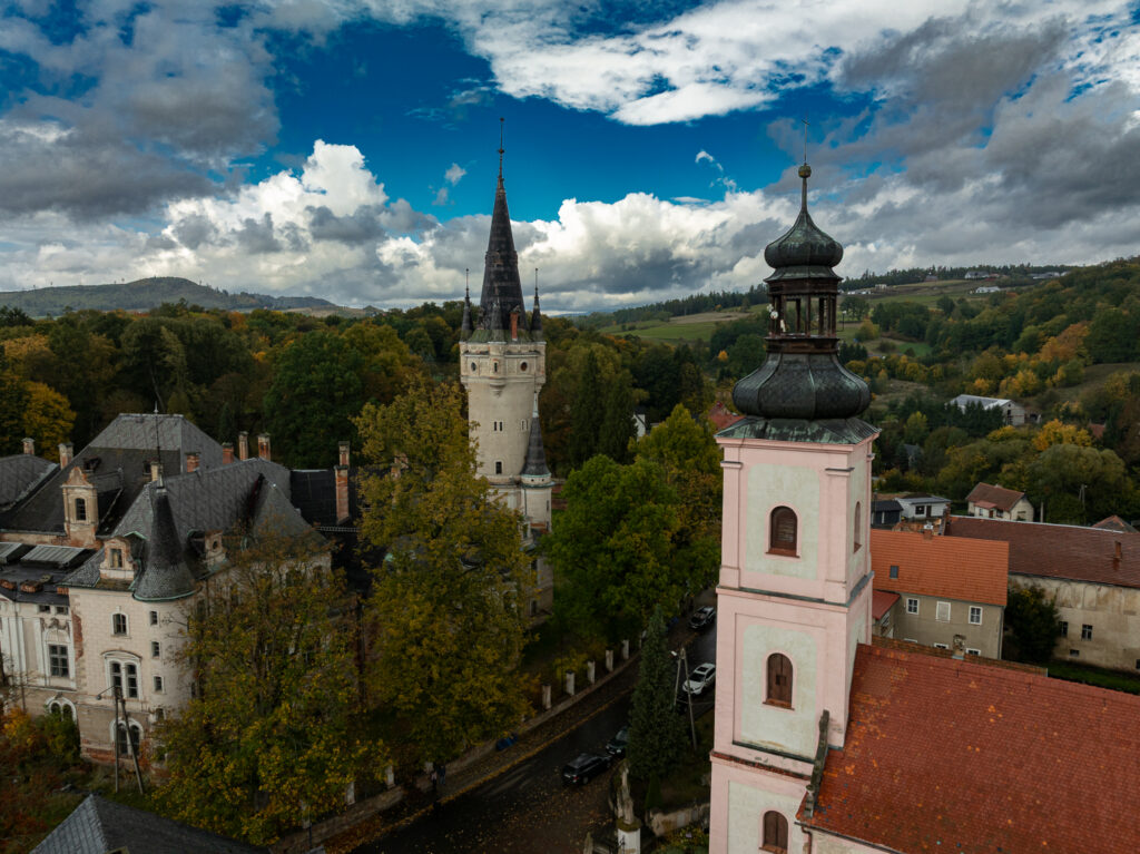 Jasny kościół z wieżą otoczony drzewami sfotografowany z góry.