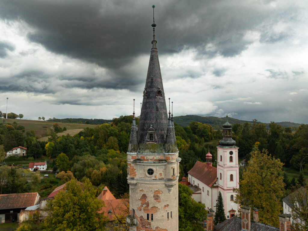Widok z drona na kościół, drzewa i zabudowę miejscowości.