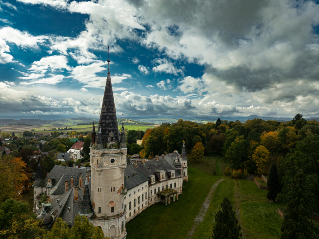 Zabytkowa wieża i historyczna zabudowa otoczona zielenią widziane z drona.