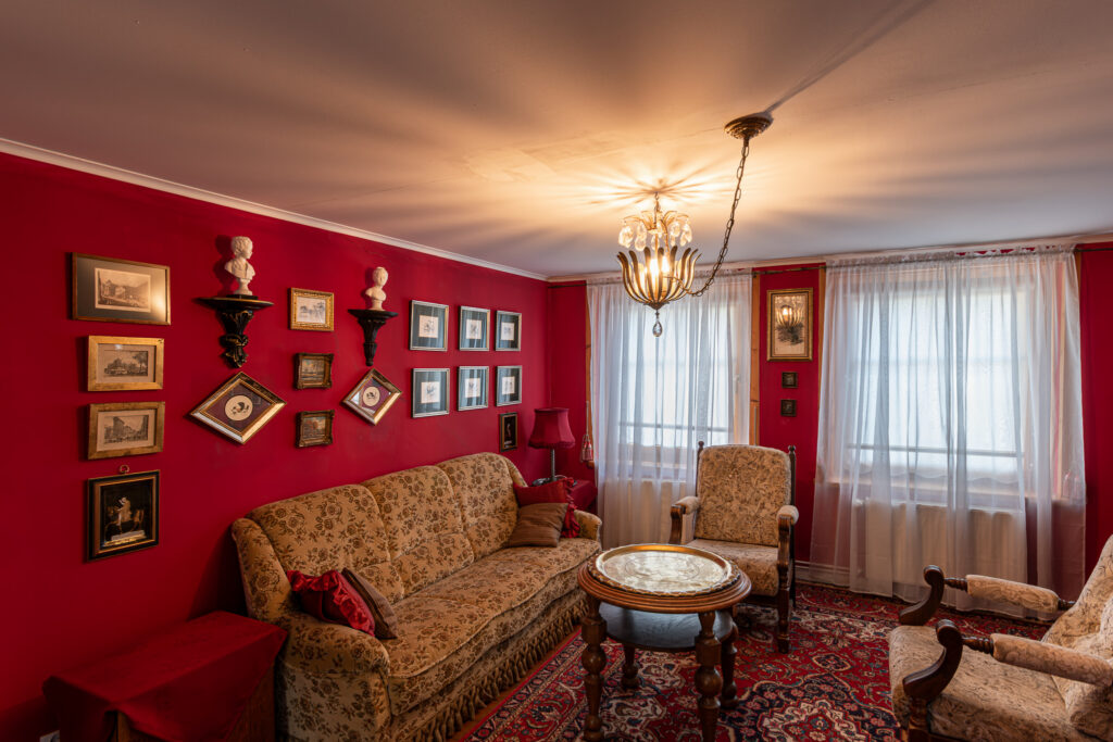 Czerwony salon w Pałacu Goworów z ozdobnym żyrandolem i historycznym wystrojem.