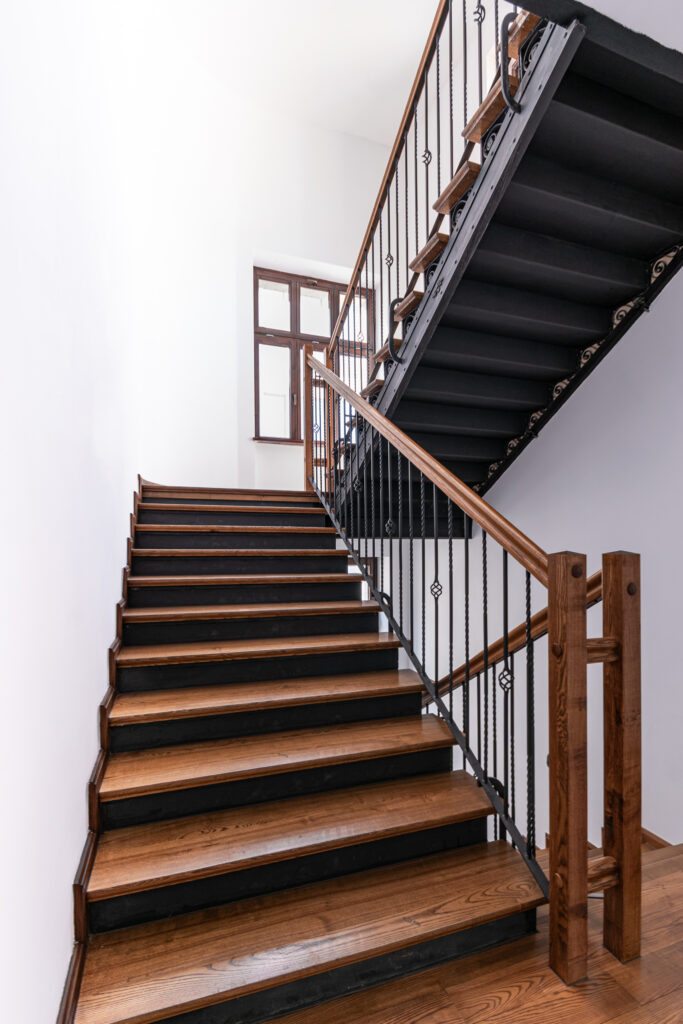 Drewniane schody z ciemną balustradą w kamienicy.